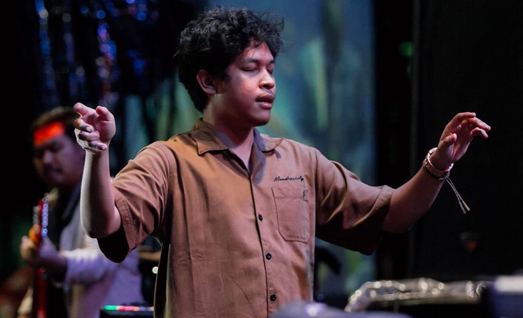 Baskara Putra atau Hindia mengenakan kemeja coklat sedang ada di atas panggung